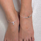 Silver anklets on feet against a neutral background