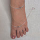 Silver anklets on a foot against a neutral background