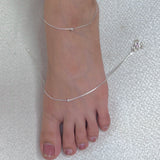 Silver anklet on a foot against a textured white background